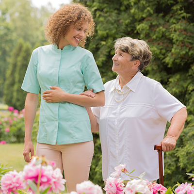 Nurse walking with an elderly woman outside in a garden. Beaver Dam Community Hospital at home care program