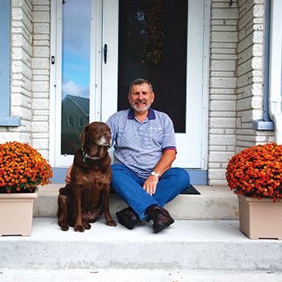 portrait of a former Hillside Home Care patient sitting outside his home with his dog
